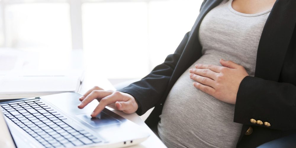 Беременная женщина, сидящая за столом с компьютером